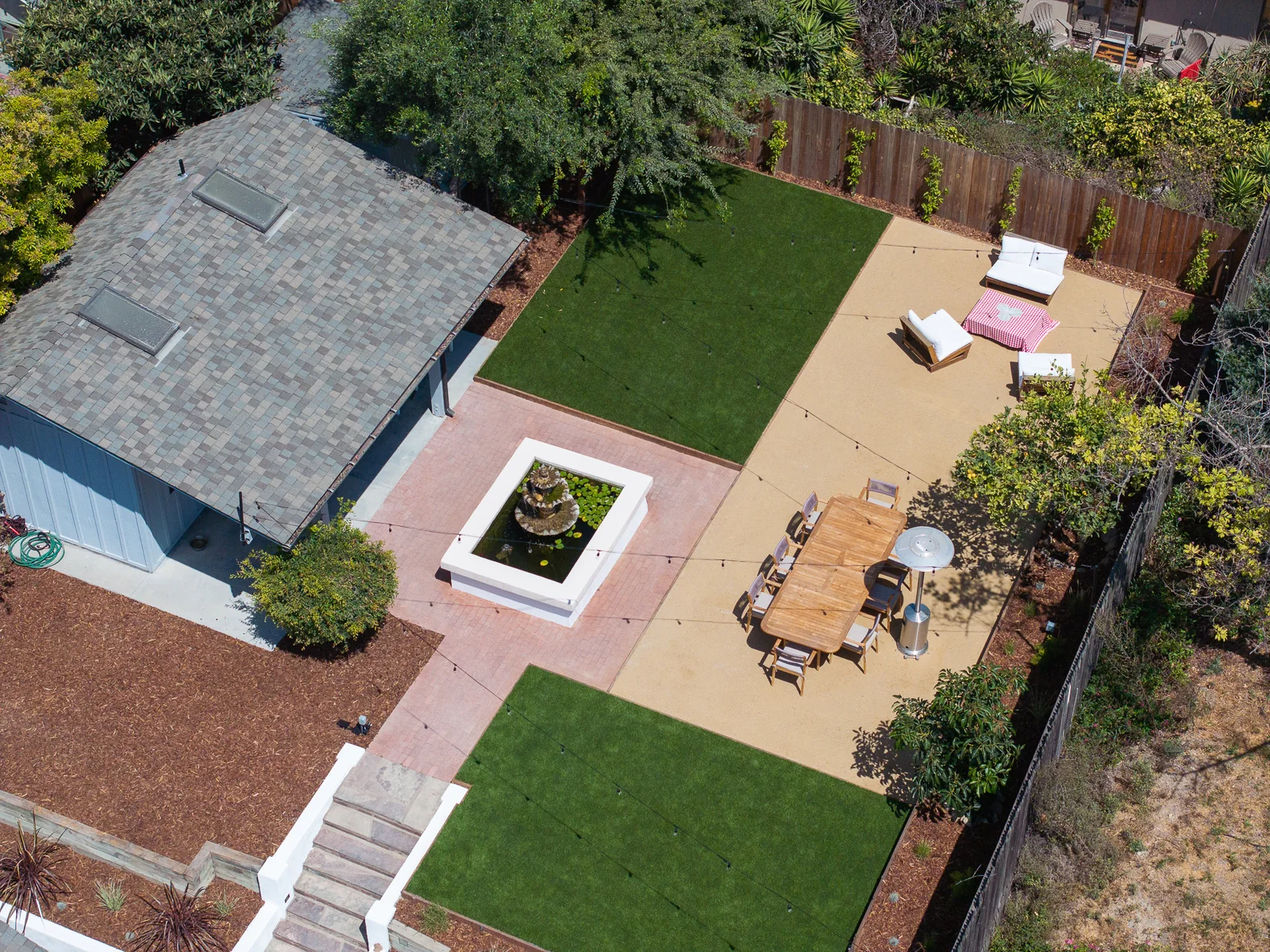 Aerial view of the finished backyard showing two turf panels flanking a decomposed granite patio, with the brick paved lily pond at the center