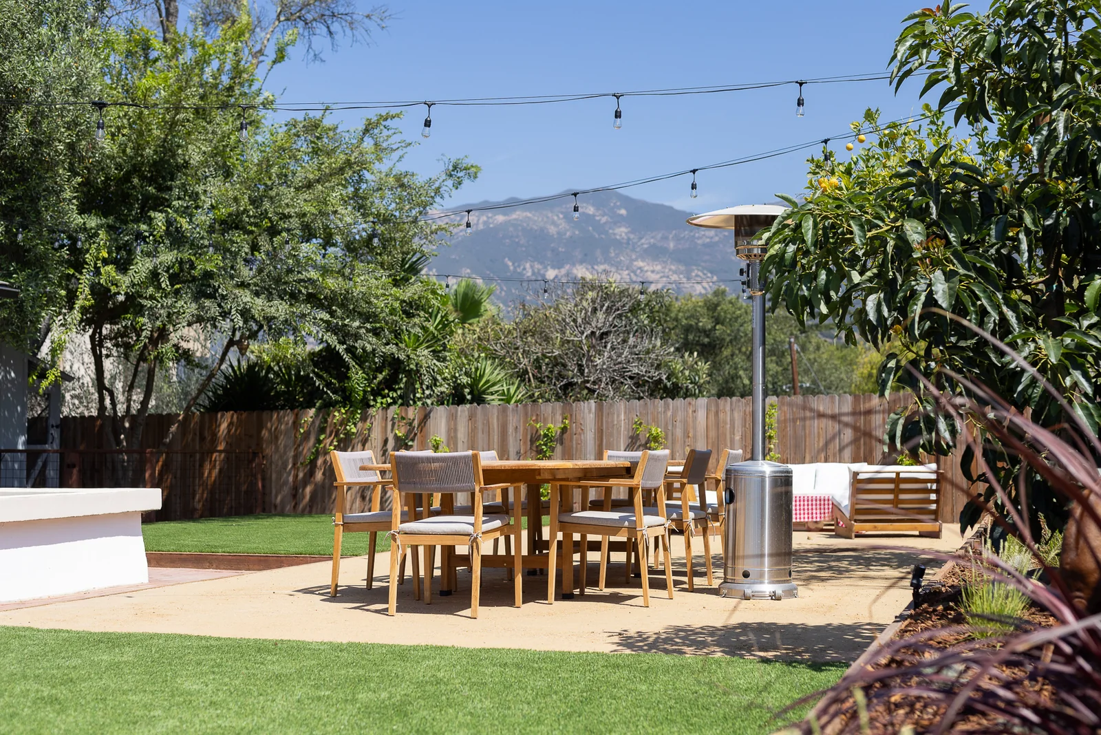 Teak dining table and patio heater on the decomposed granite terrace, framed by citrus and avocado